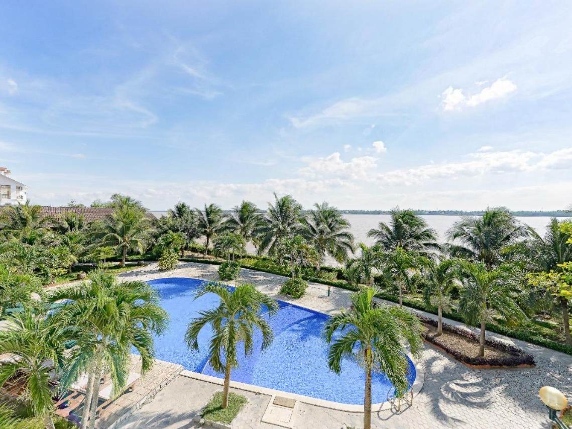 Free-form blue pool with palm islands and sun loungers beside a wide river