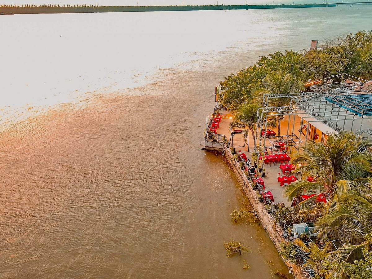 Aerial view of red-clothed tables laid out on a riverside terrace beside wide brown water