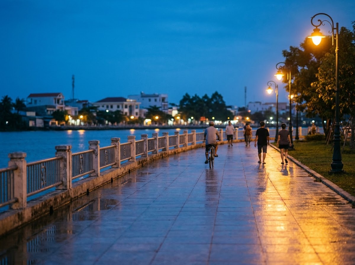 Riverside promenade at dusk with street lamps, palm trees and people walking beside the water