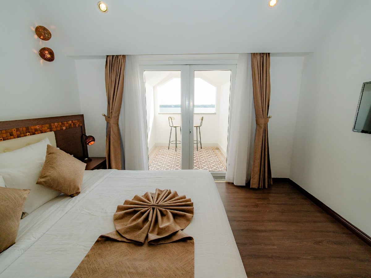 Bett mit gefaltetem Handtuchfächer, Holzboden und offener Tür zu einem Balkon mit zwei Stühlen
